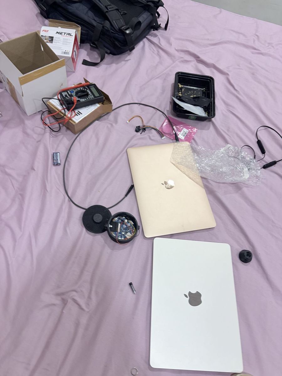 Bed covered with laptops, a multimeter, cables and an open case with the board inside